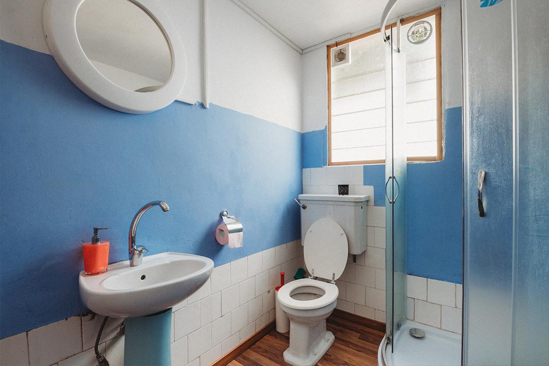 A photo of a bathroom with a toilet, sink and glass shower cubicle, with blue walls