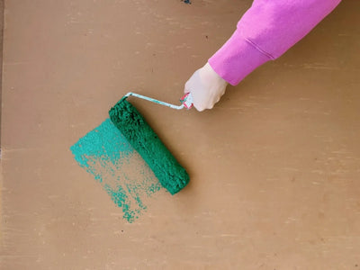 A paint roller with green paint being painted onto a wooden board by a hand